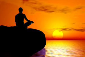 Man sitting meditating on a rock with the sun setting in the distance