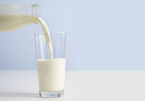 Milk being poured from a glass bottle into a glass