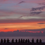 A group of friends sitting on the beach watching the purple sunset