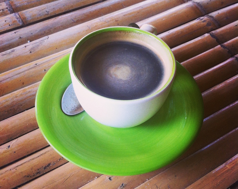 Black coffee in a green cup with saucer on bamboo table
