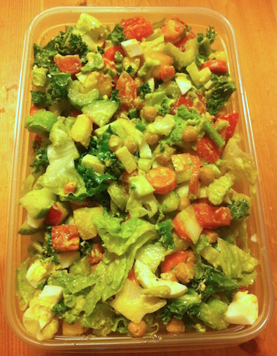 Salad with celery, tomato, kale, boiled eggs, fruit, olive oil, beans and more in a tupperware container