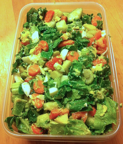 Salad with celery, tomato, kale, boiled eggs, fruit, olive oil, beans and more in a tupperware container
