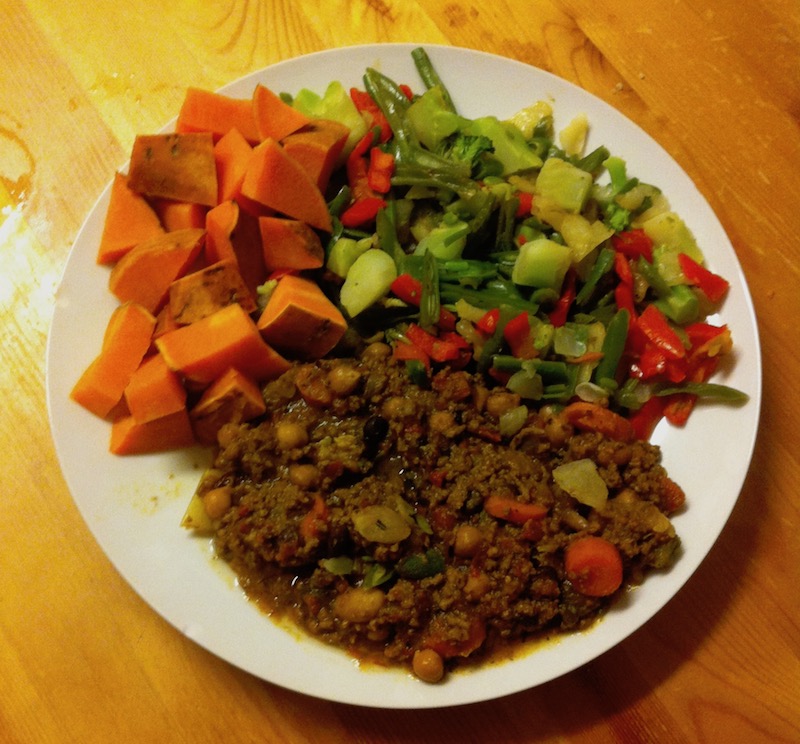 Plate with homemade chilli, orange sweet potatoes and mixed vegetables on a wooden table